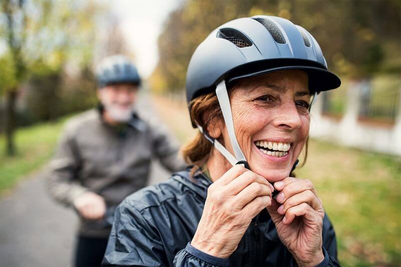 Lady cycling and putting on a helmet.